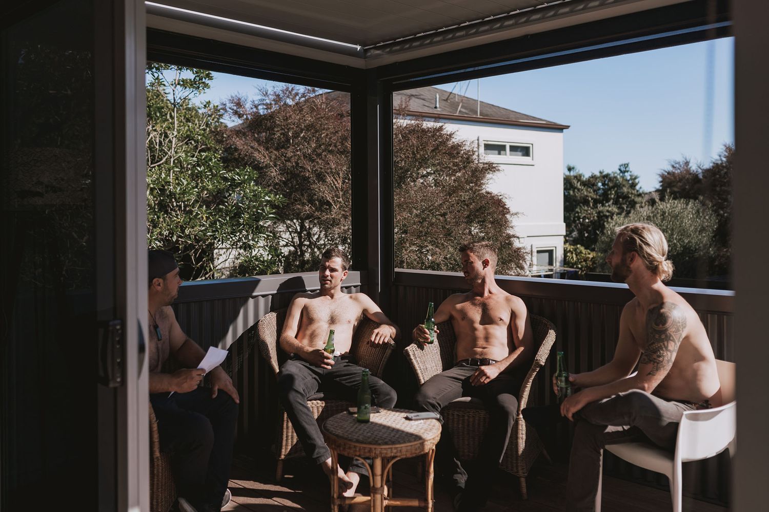 Small group of friends relaxing together at a modern poolside patio area under an outdoor canopy on a sunny day.