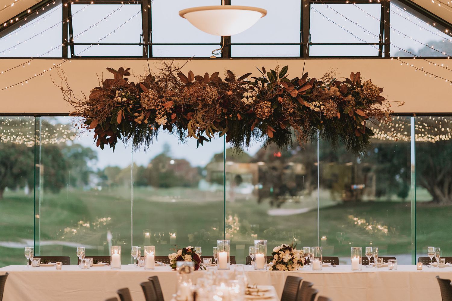 A panoramic view of a rustic barn wedding reception venue decorated with warm lighting and exposed wooden beams.