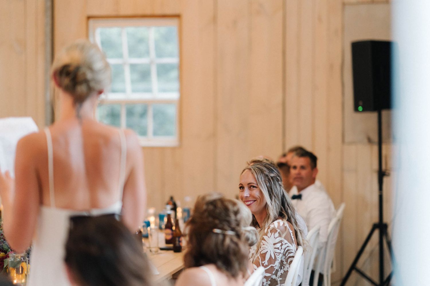 Reception guests gather at elegantly set tables in a rustic wooden barn venue during a wedding celebration.