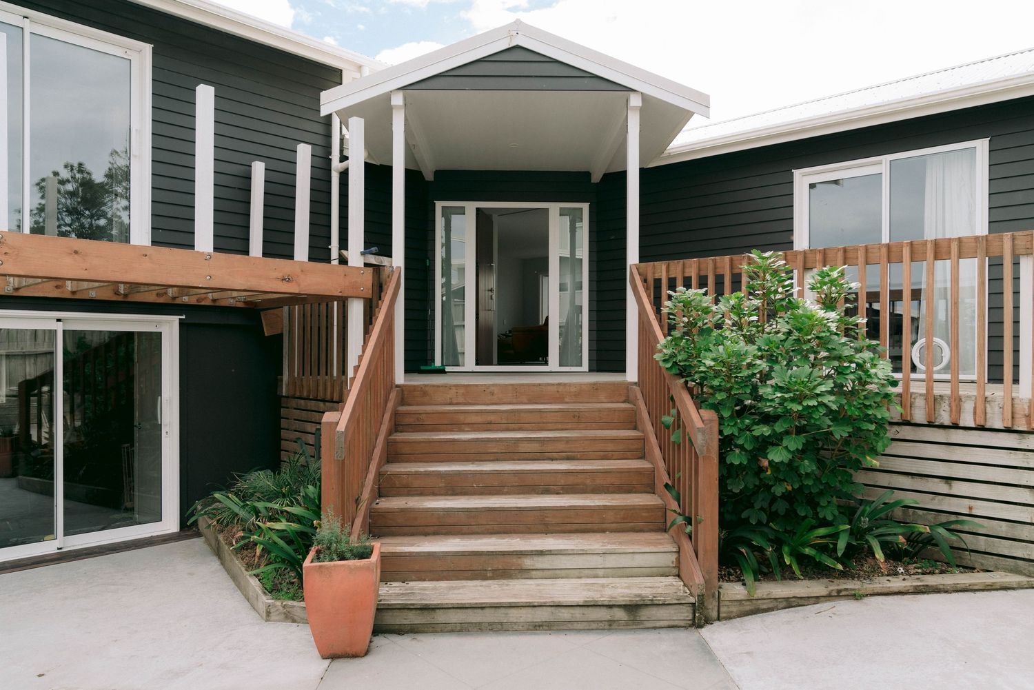 Modern home entrance with brown wooden stairs and glass front door features twin side panels and lush garden accents.