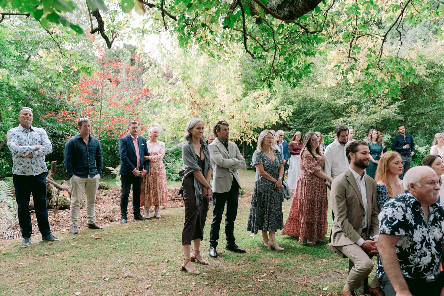 Wedding guests line up in a wooded outdoor setting creating a receiving line formation.