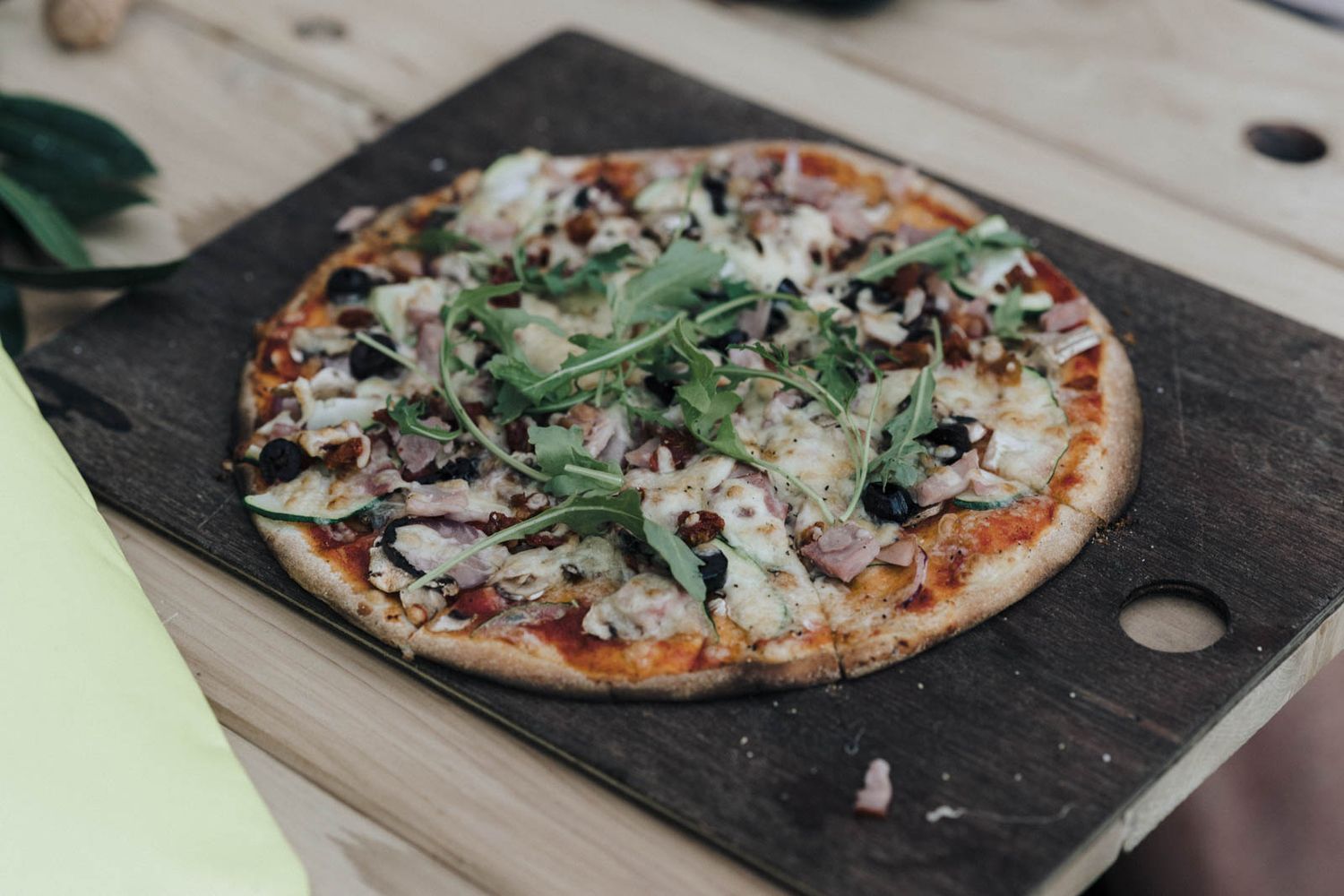 Homemade pizza topped with mushrooms, red onions, and fresh herbs sits on a rustic wooden cutting board.