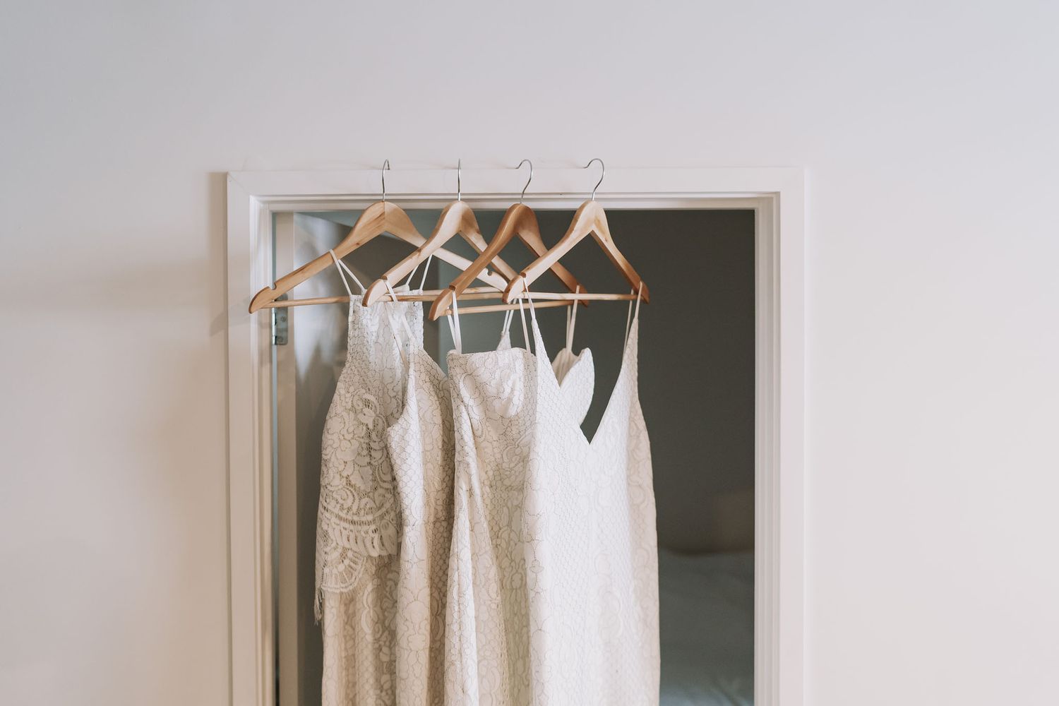 Four elegant bridal or formal dresses in shades of white and cream hanging on wooden hangers in a closet.