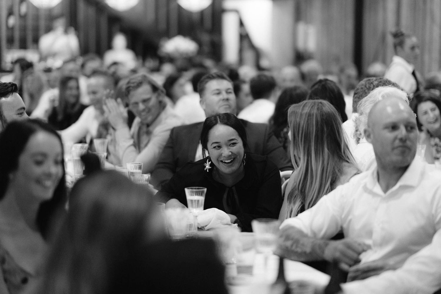 Wedding reception guests enjoying dinner at long tables under string lights in an outdoor setting.