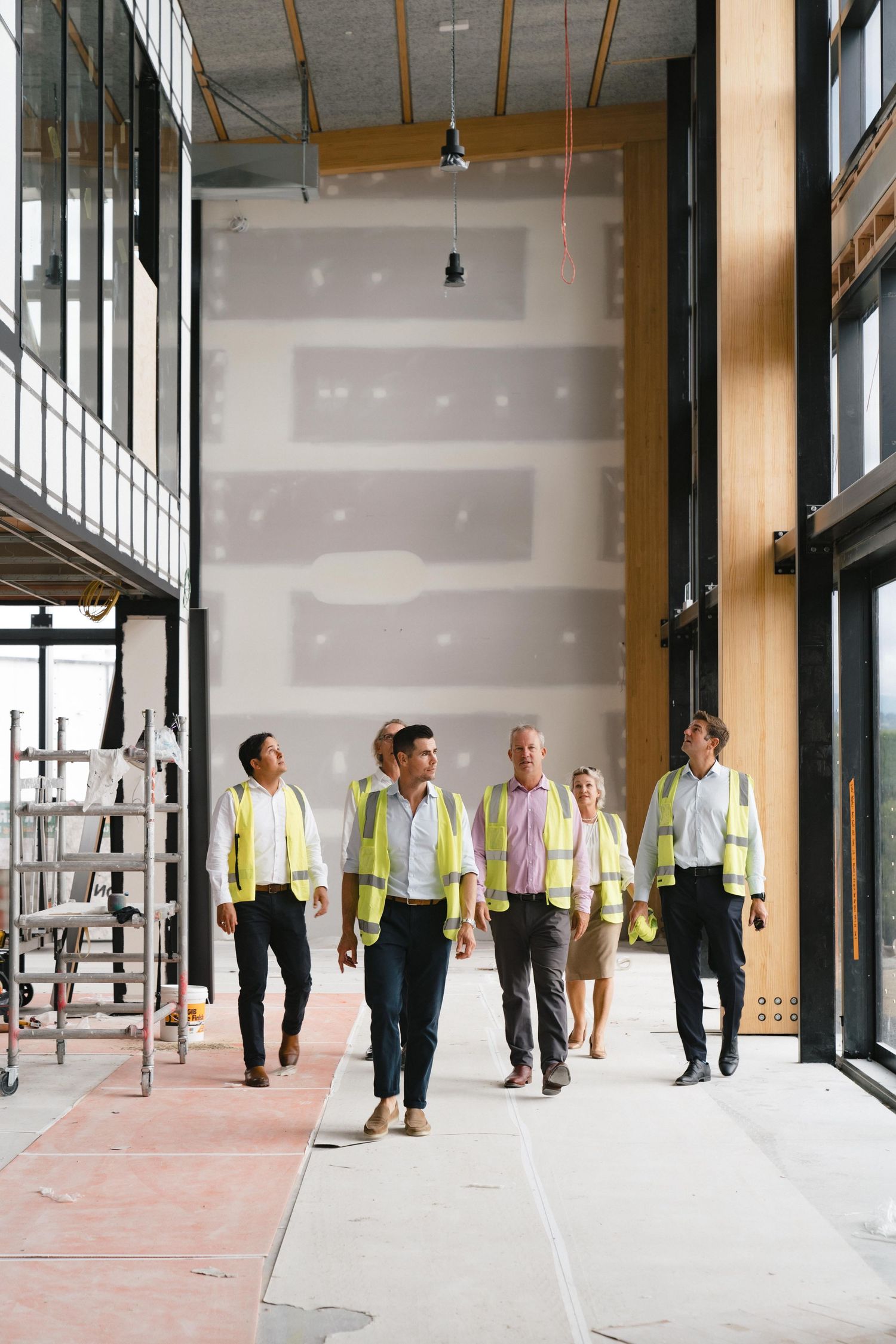 Group of professionals in safety vests inspecting a construction site with tall ceilings.