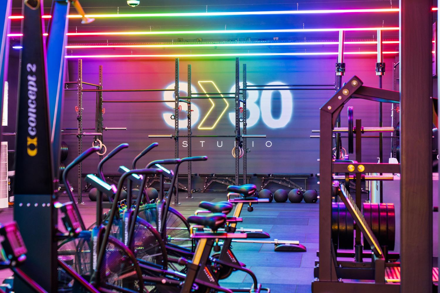 Modern gym interior with colorful rainbow LED lighting and exercise equipment silhouetted against neon wall.