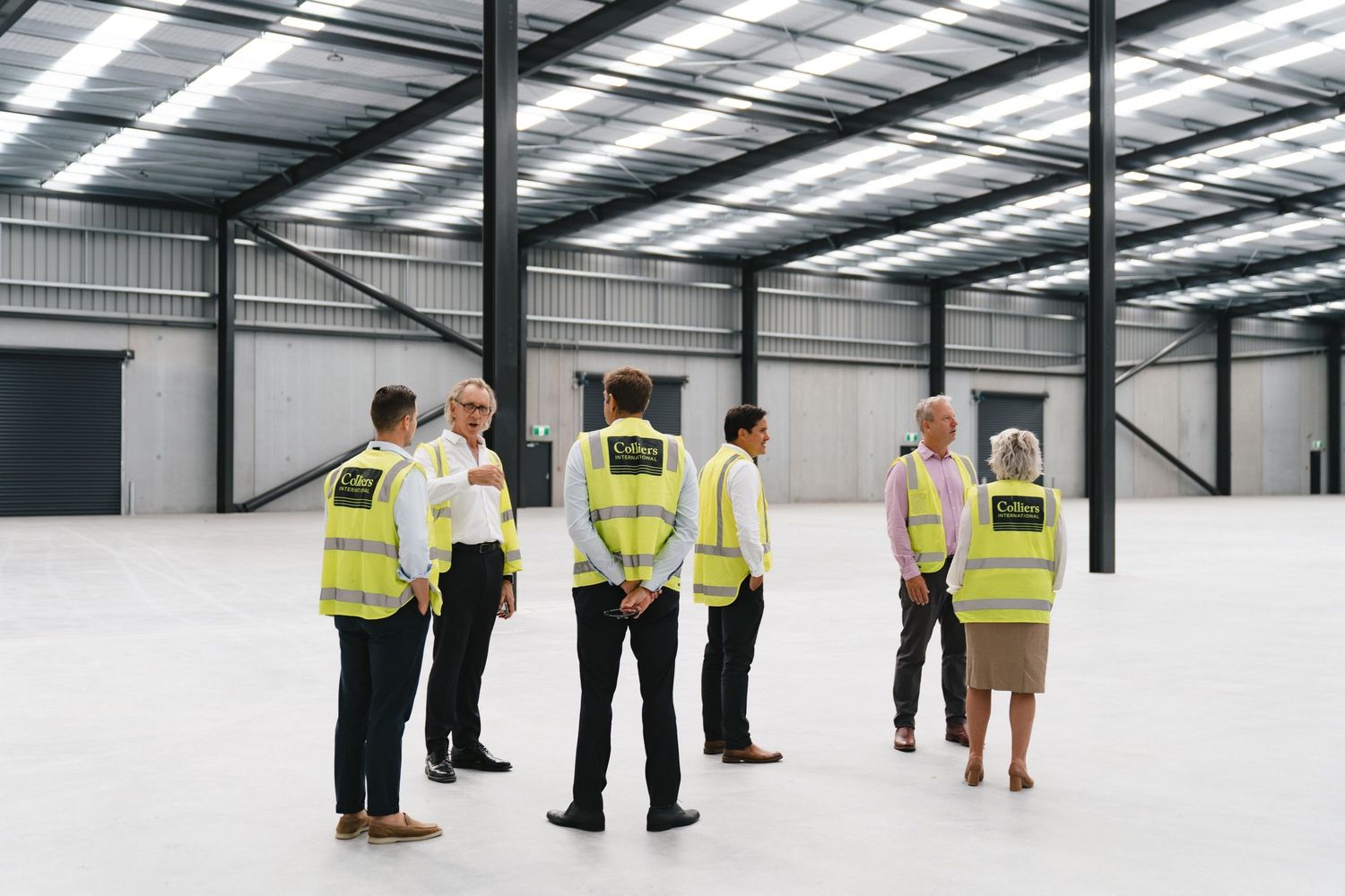 Group in safety vests inspecting empty industrial warehouse space during a site visit.