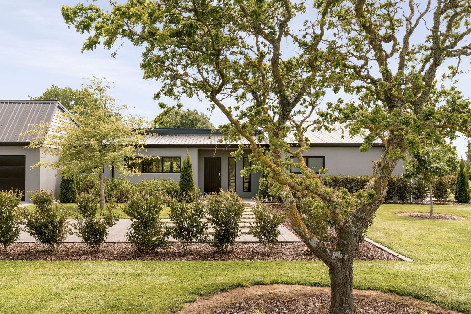 Modern farmhouse exterior features white siding, black trim, and manicured landscaping with mature trees.