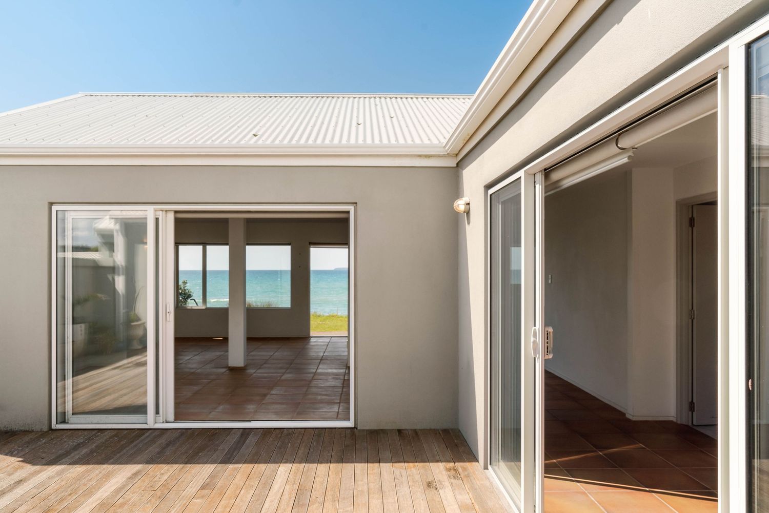 Modern beach house interior with sliding glass doors opening to a wooden deck and ocean views.
