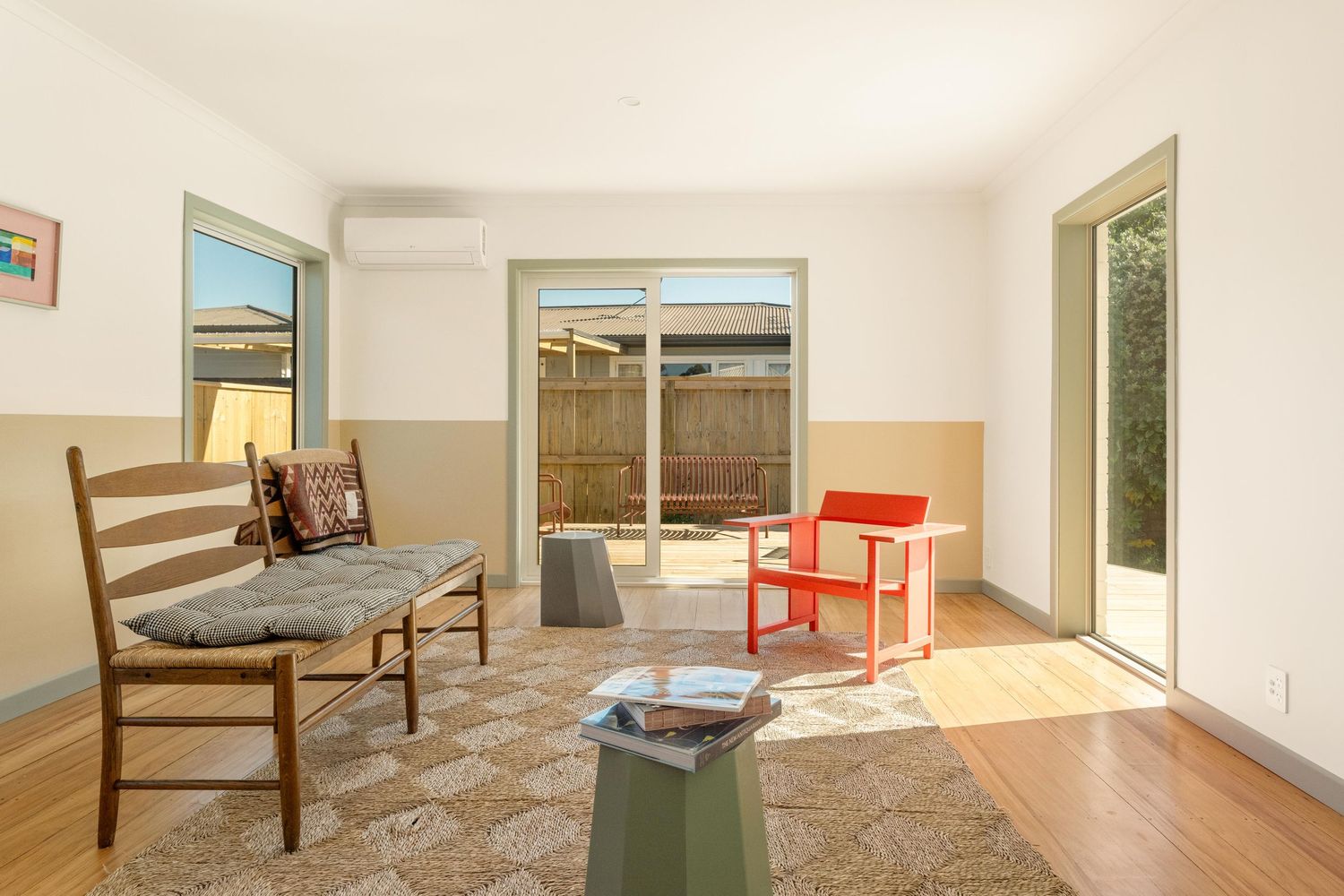 Modern minimalist living room with wooden chair, red accent chair, and sliding glass door to patio.