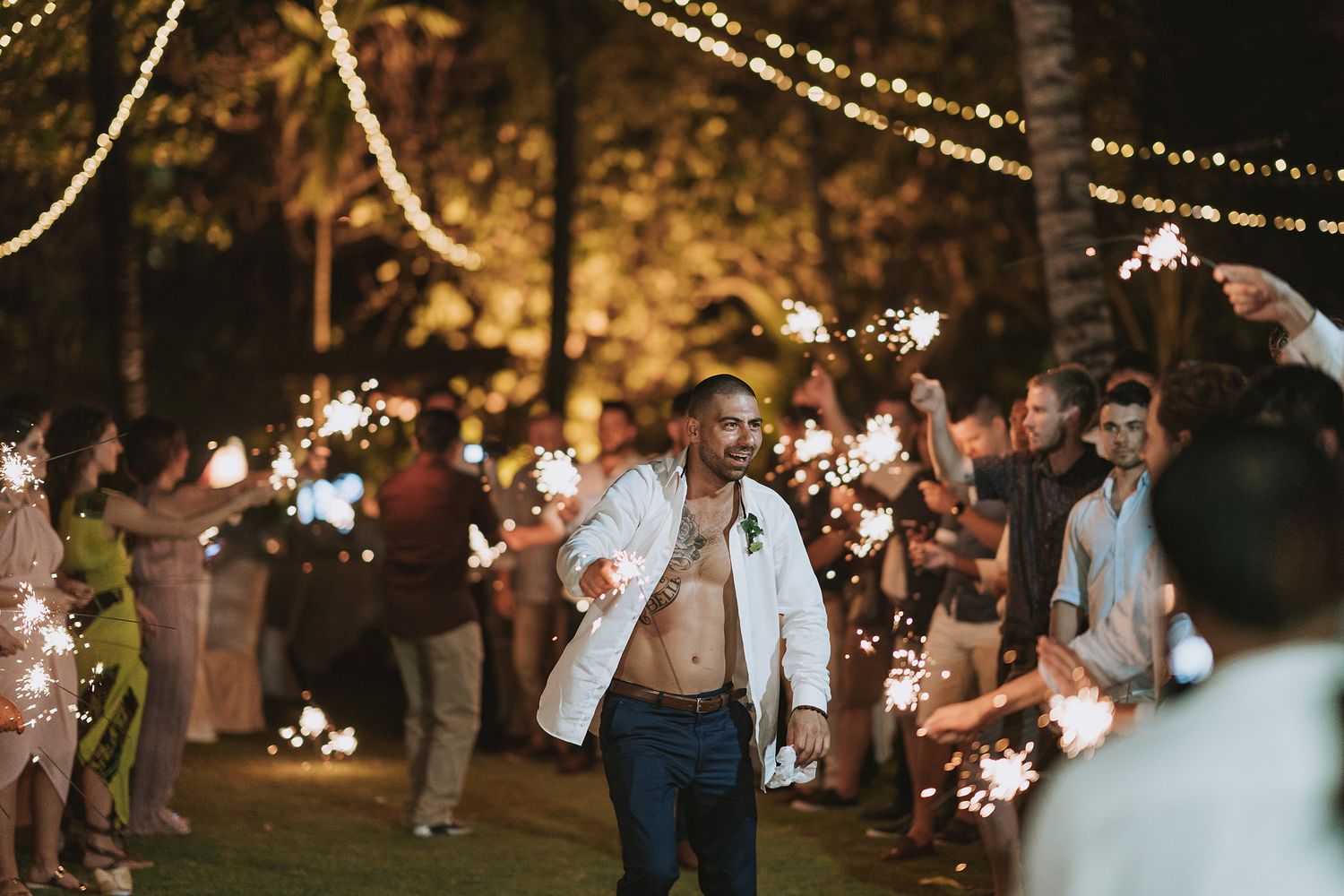 Wedding guests celebrate with sparklers during an evening outdoor reception.