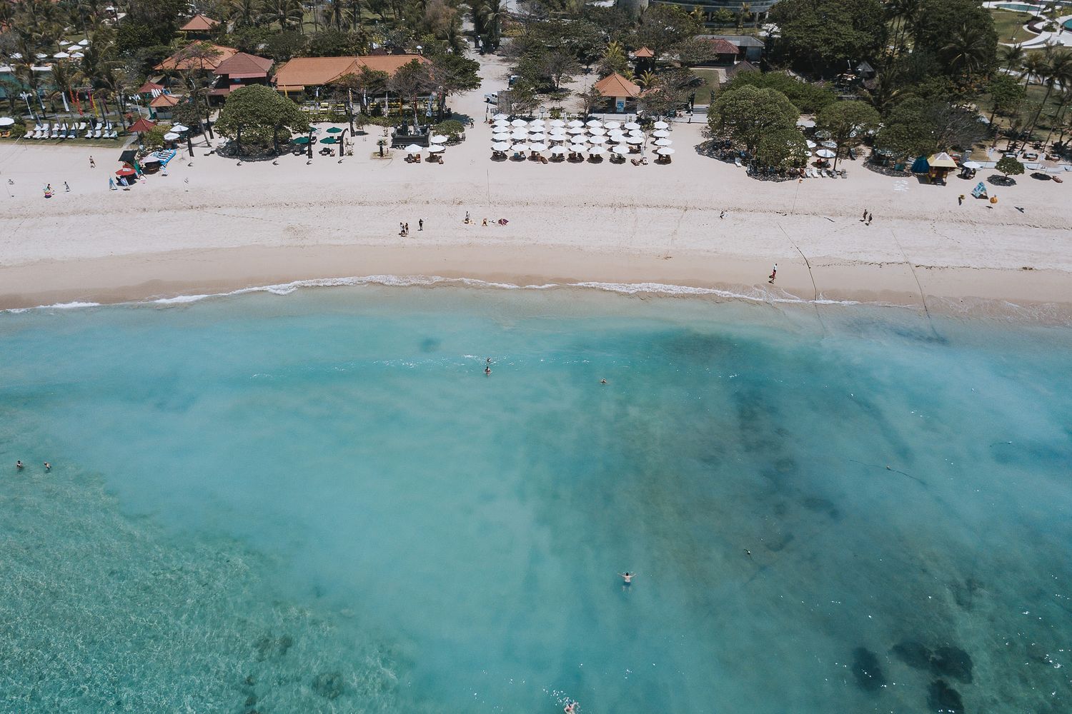 Aerial view of a pristine Caribbean beach with turquoise waters, white sand, and beach chairs under palm trees.