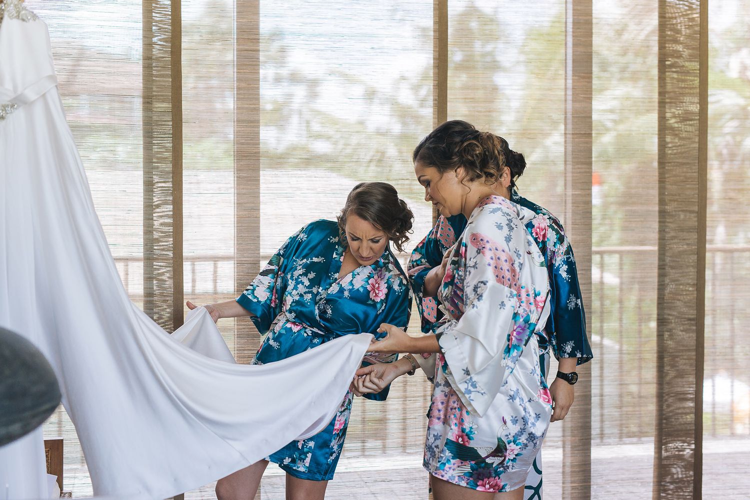 Two women in floral print robes help arrange fabric in a bright indoor setting.