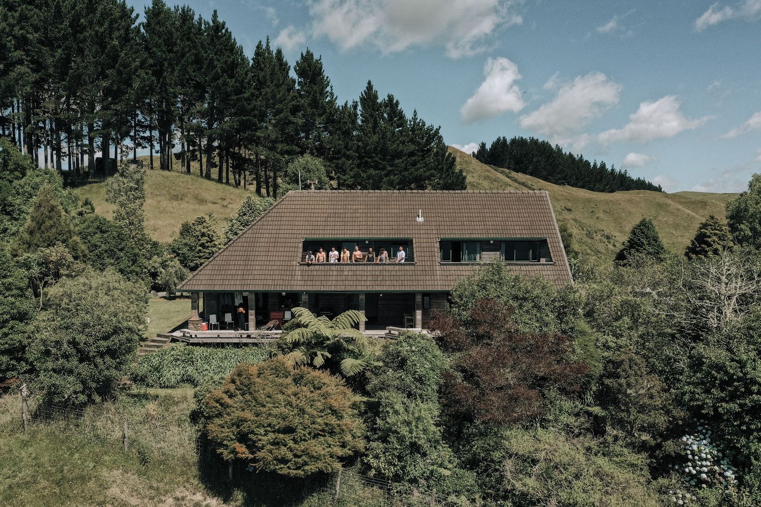 Modern wooden hillside lodge nestled among pine trees and green slopes in a scenic mountain landscape.