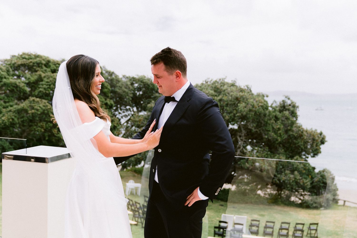 A bride and groom share a tender moment on a balcony overlooking green trees on their wedding day.