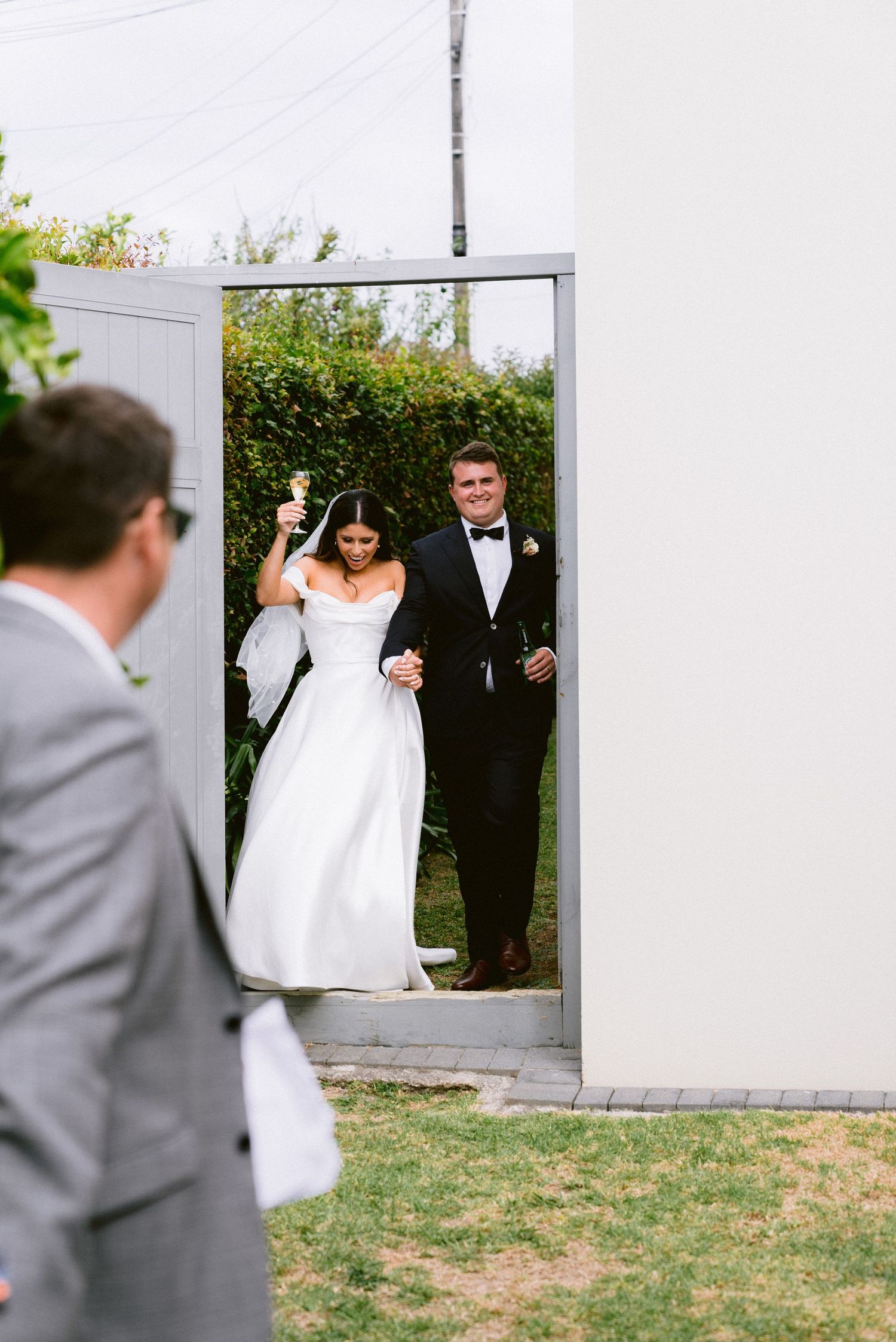 A couple makes their entrance through a white garden gate during their wedding celebration.