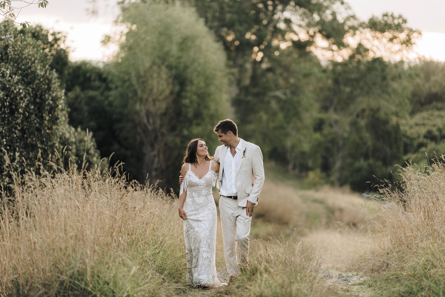 Romantic wedding couple walking along nature path through tall grass.