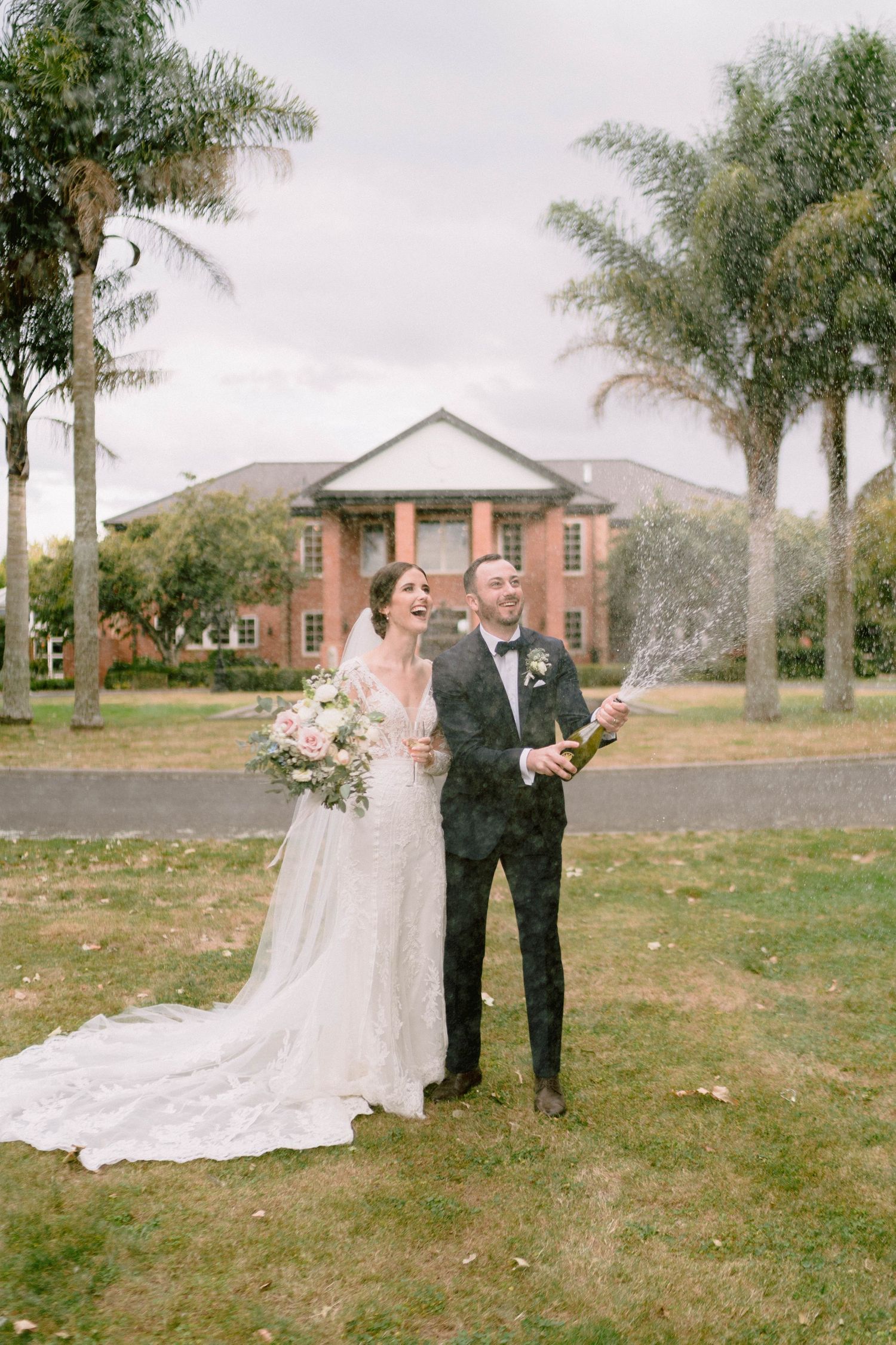 A wedding ceremony taking place outdoors with palm trees and a brick building in the background.