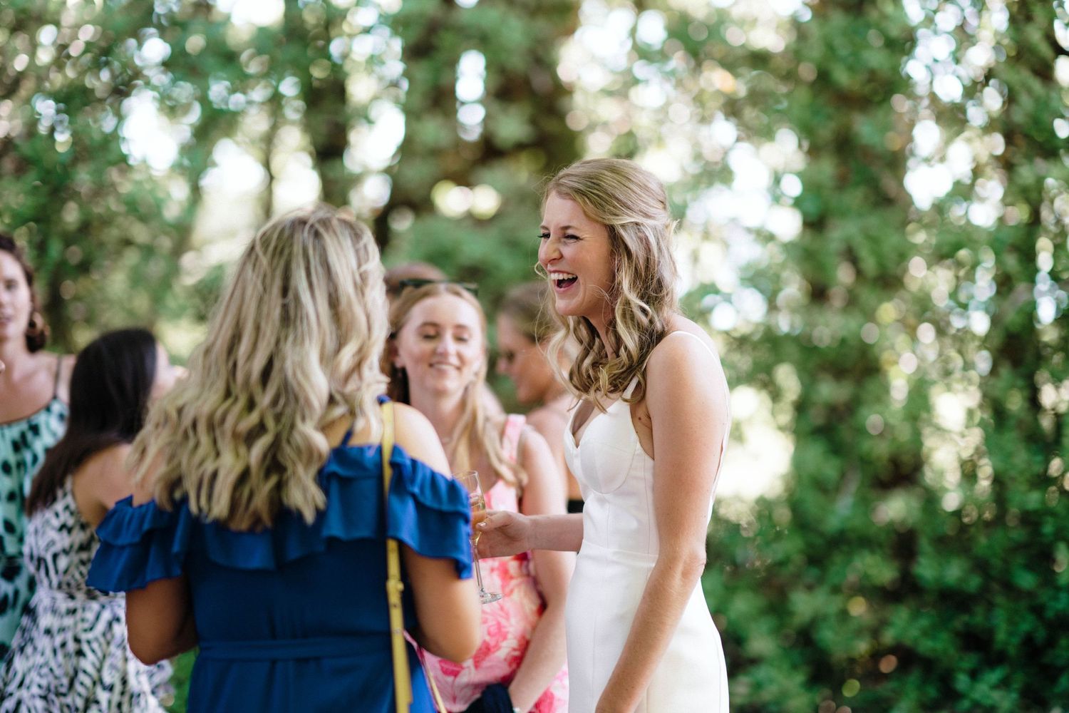 Guests celebrating at an outdoor wedding reception under tree cover.