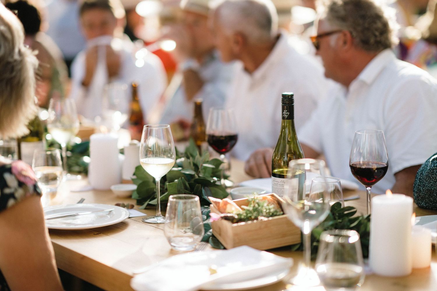 An elegant outdoor wedding reception table set with wine glasses, candles and greenery decorations.