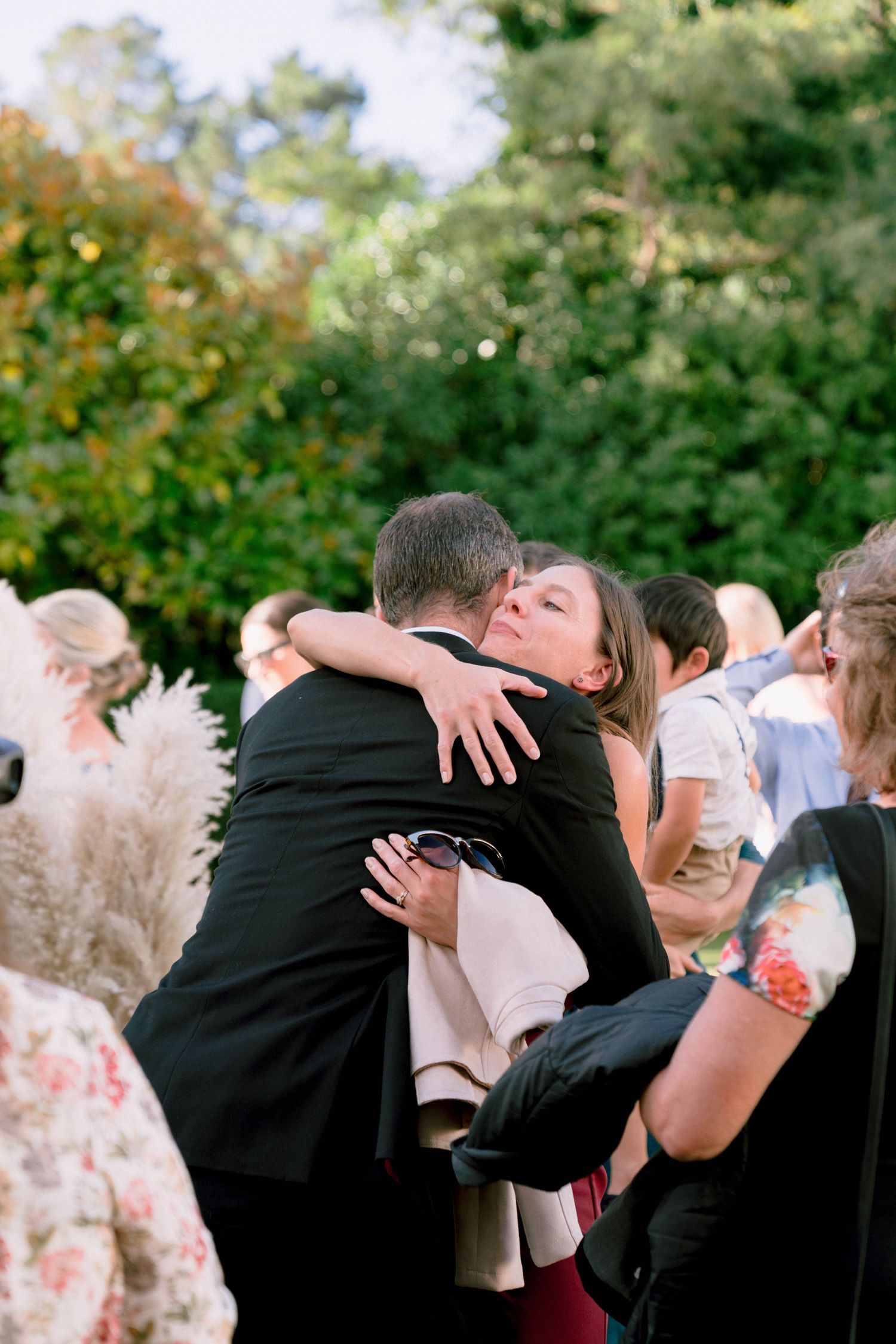 Emotional embrace during outdoor wedding celebration with guests and decorative pampas grass.