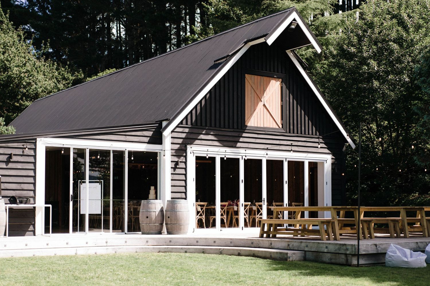 Modern black-roofed lodge with glass windows and wooden deck surrounded by forest.