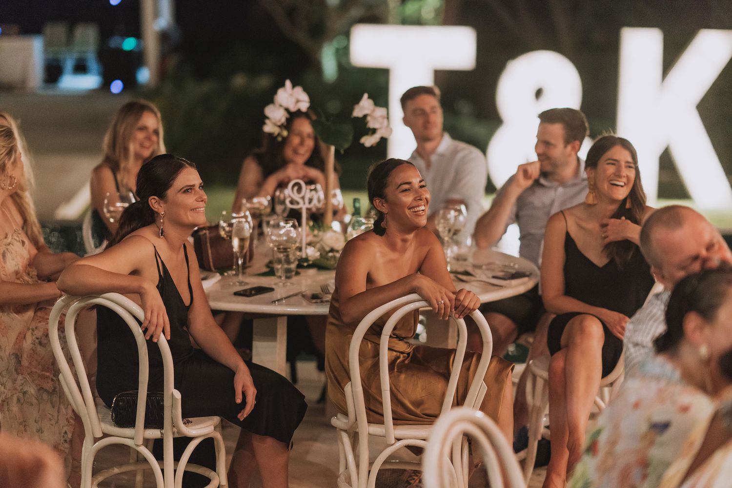 Wedding reception guests enjoy an evening celebration at tables under outdoor lighting.