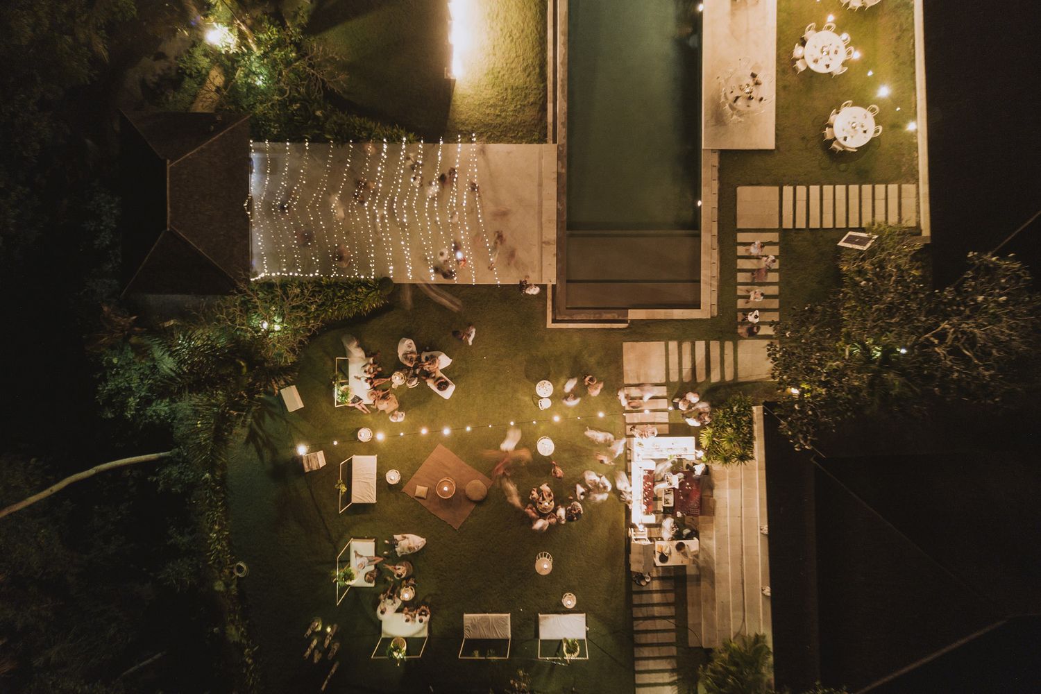 Aerial view of an illuminated outdoor wedding reception venue at night with string lights.