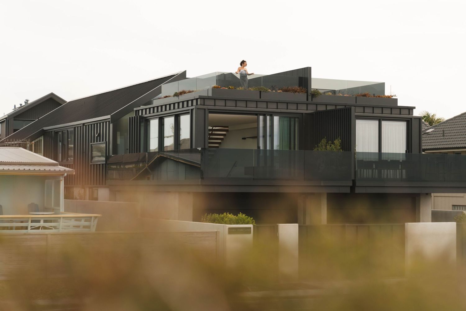 Modern beachfront architecture with black exterior and white fencing along coastal landscape.