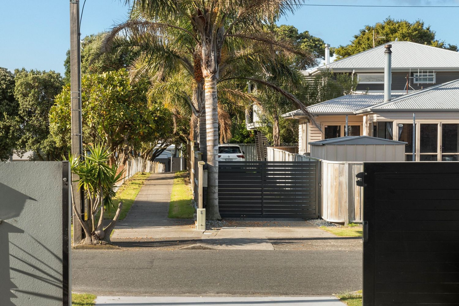 Modern suburban street with black gate entrance, palm trees and residential homes on a sunny day in Queensland.