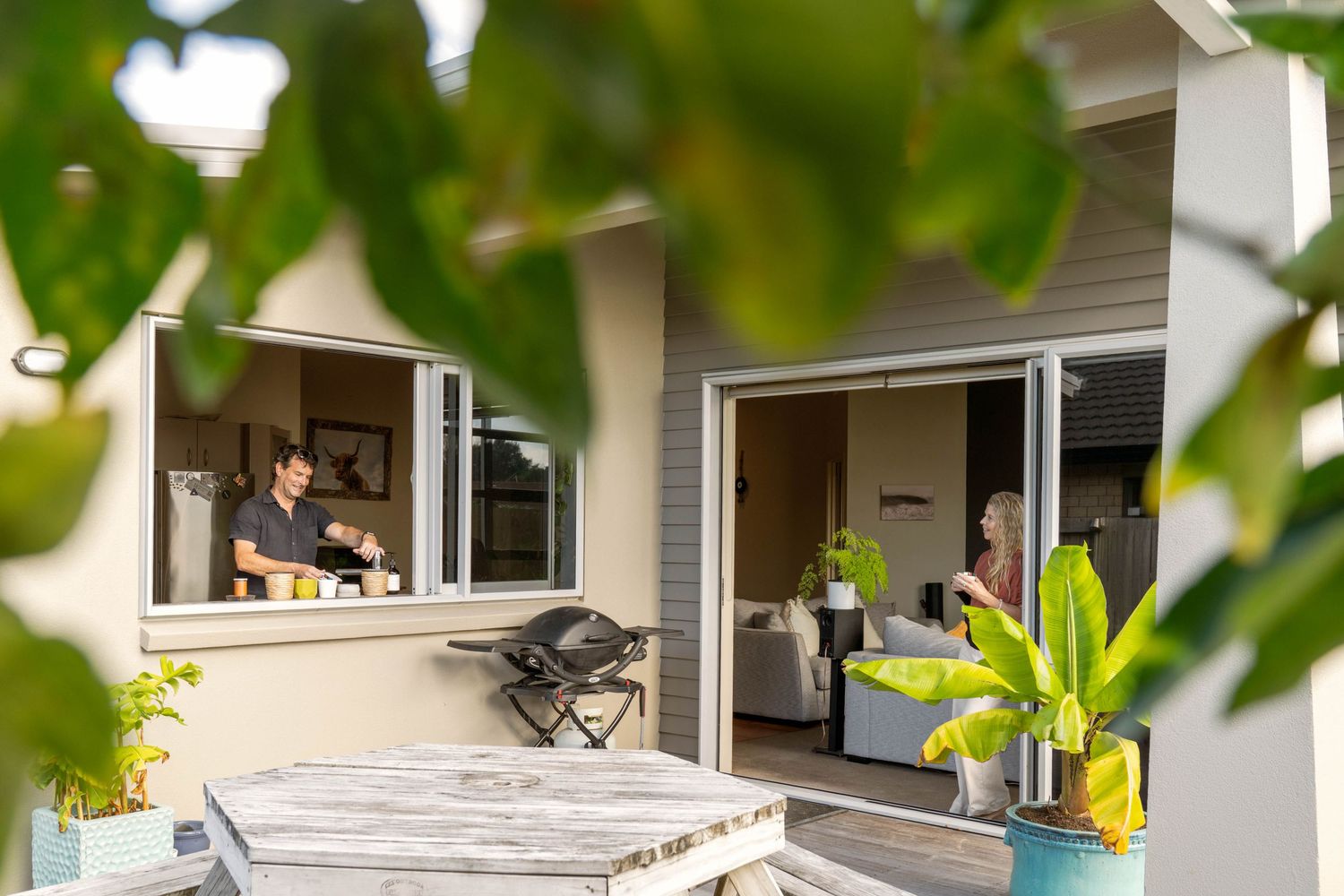 Modern home exterior with sliding windows and outdoor deck framed by lush green foliage.