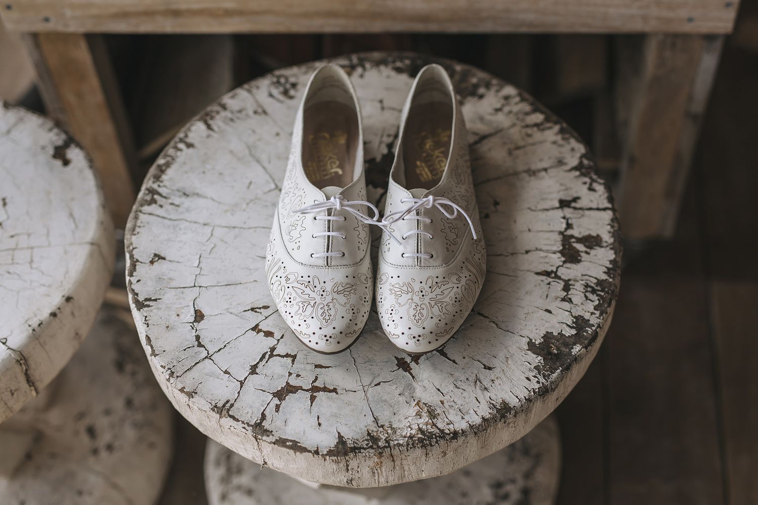 Vintage distressed white circular wooden table with peeling paint texture and white lace shoes placed on top.
