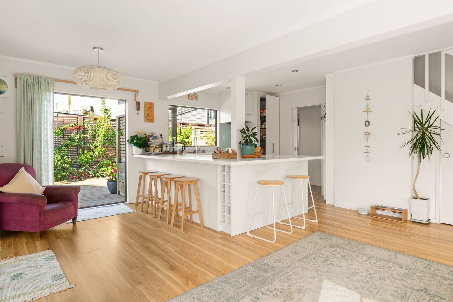 Contemporary open-concept living space with white walls, wooden flooring, and natural lighting flowing through multiple rooms.