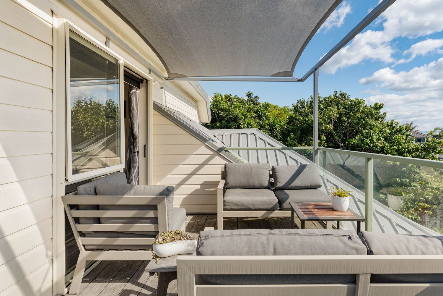 Gray rocking chair sitting on an outdoor covered porch overlooking a green summer landscape with blue skies and clouds.