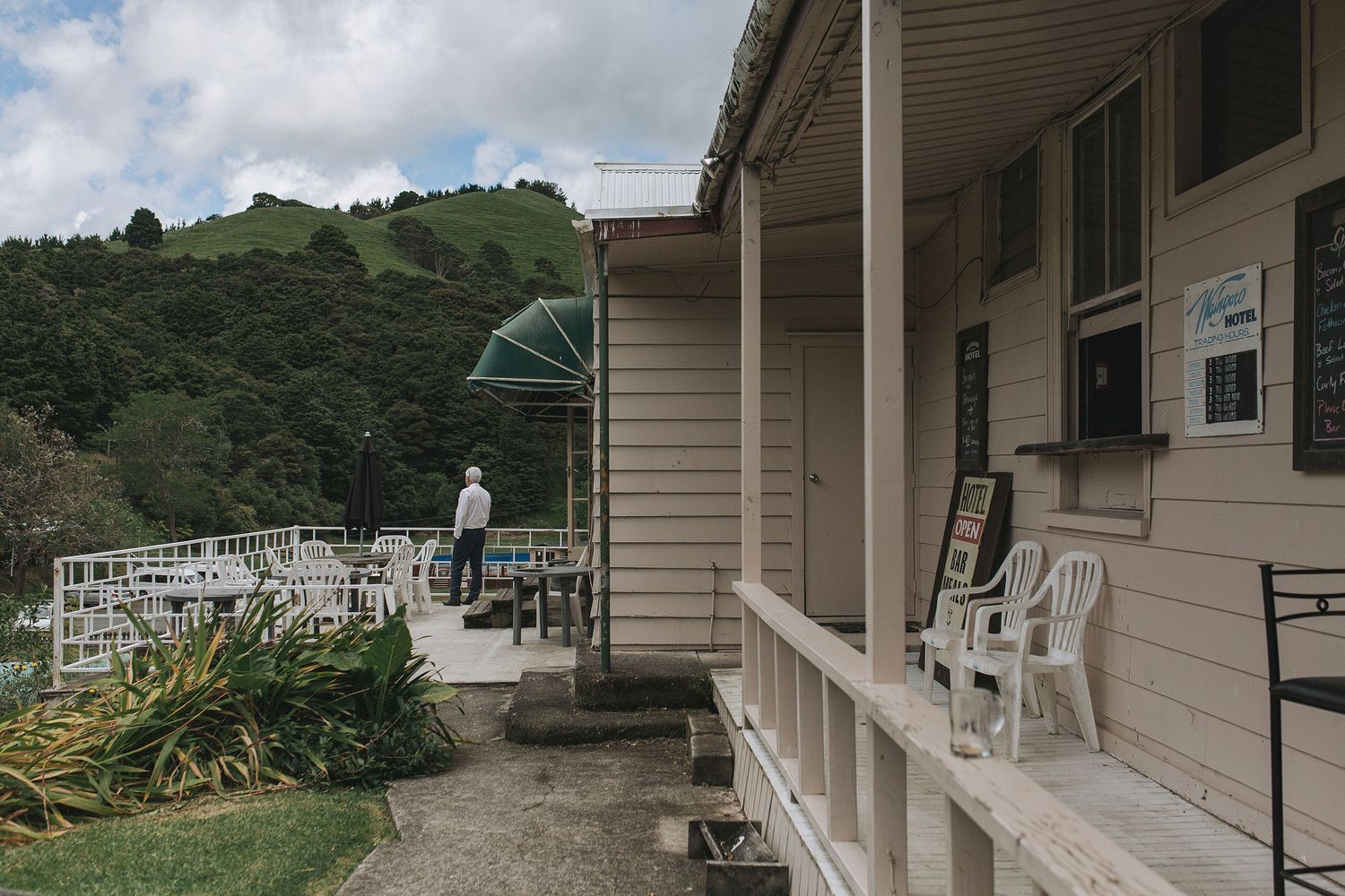 A covered porch with white chairs overlooks green hills and cemetery tombstones in a rural setting.
