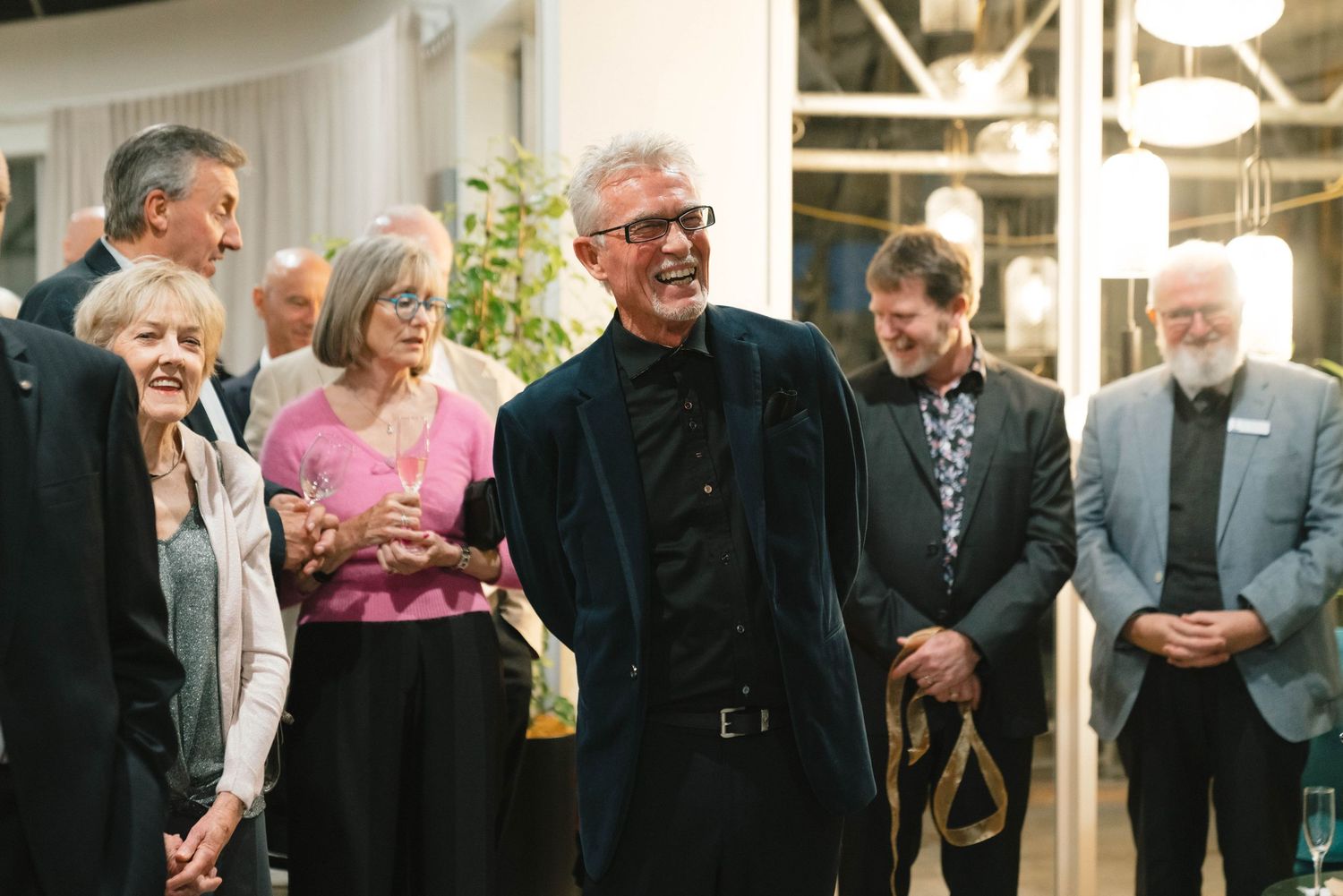 Group of attendees gathered at an indoor social event, sharing smiles and conversation.