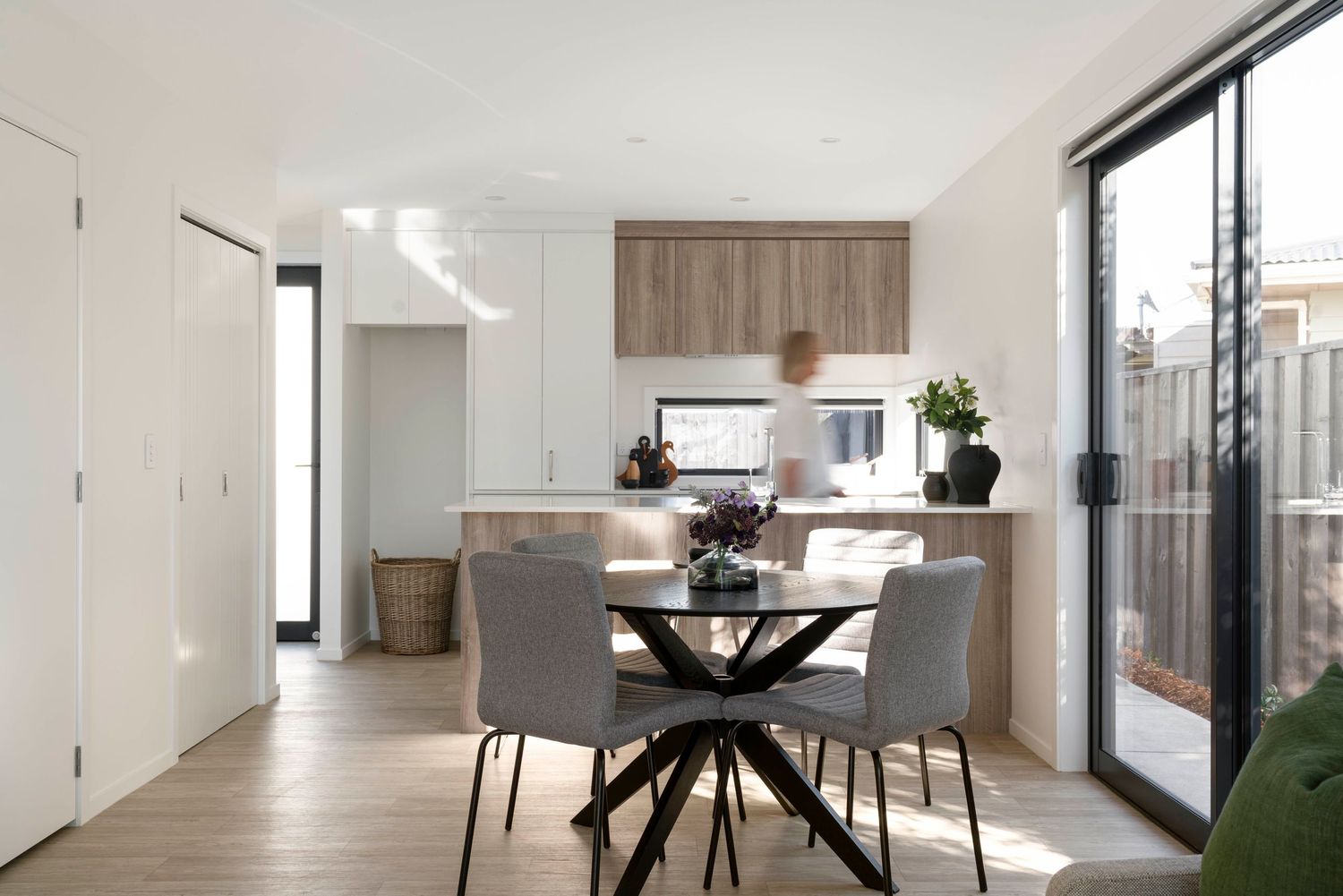 Modern open concept living room and dining area with light wood floors and minimalist white decor throughout.