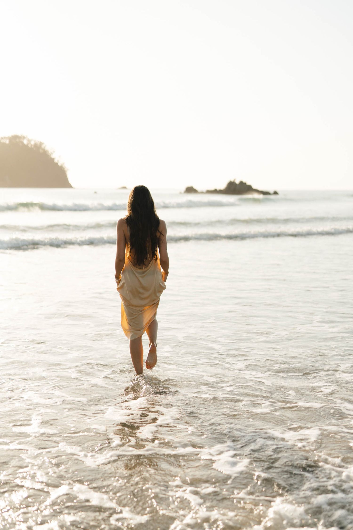 Person wading through ocean waves at beach during sunset.