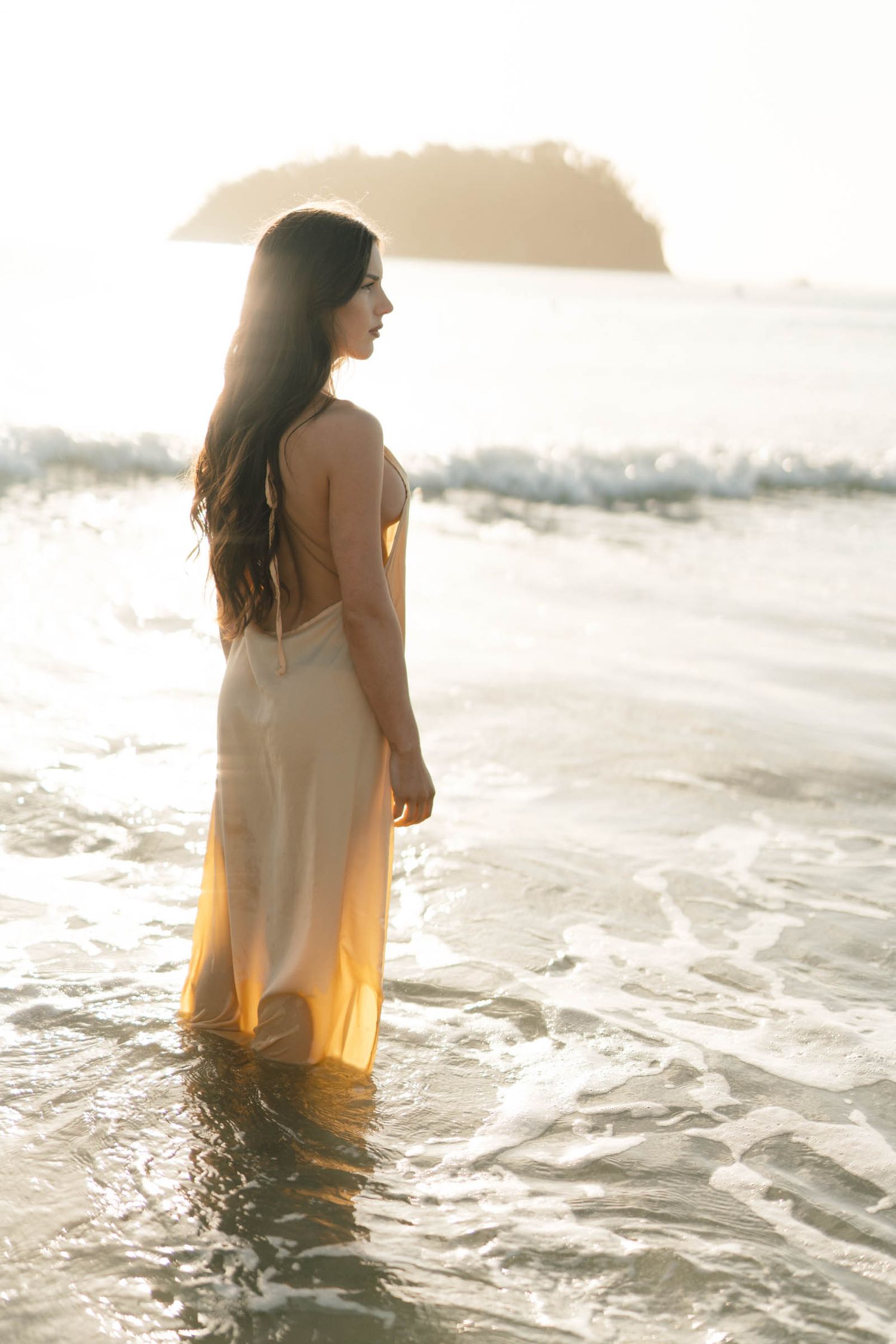 Figure in a flowing yellow dress standing in ocean waves during golden hour.