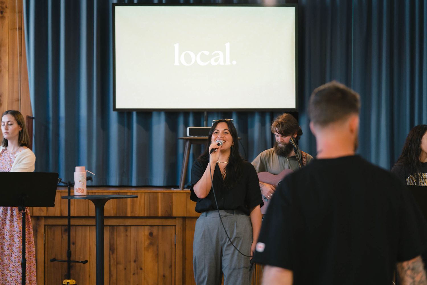 People performing music on stage with the word 'local' displayed on a screen behind them.