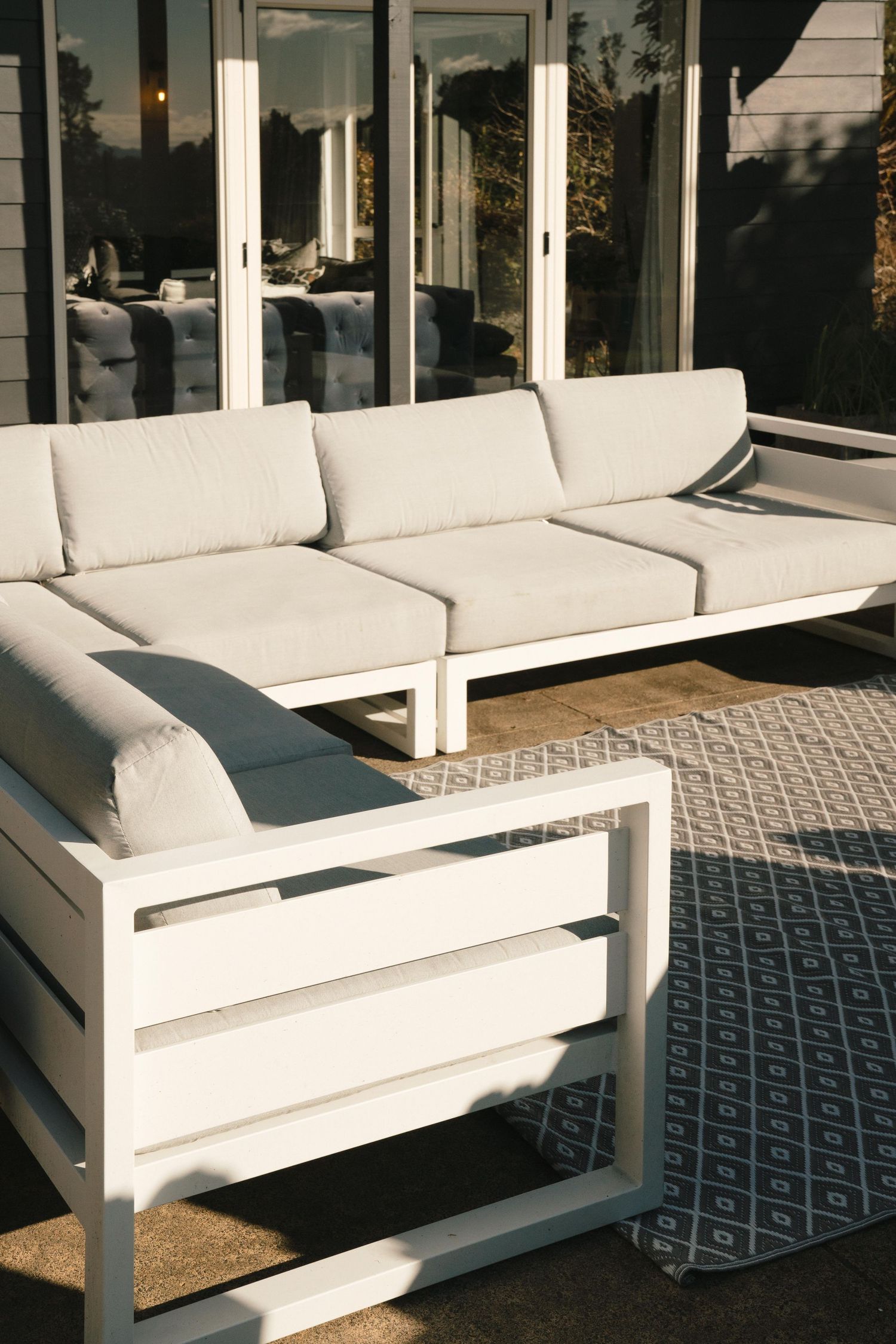 A sequence of modern white outdoor sofas with geometric patterned cushions arranged in a line on a covered patio.