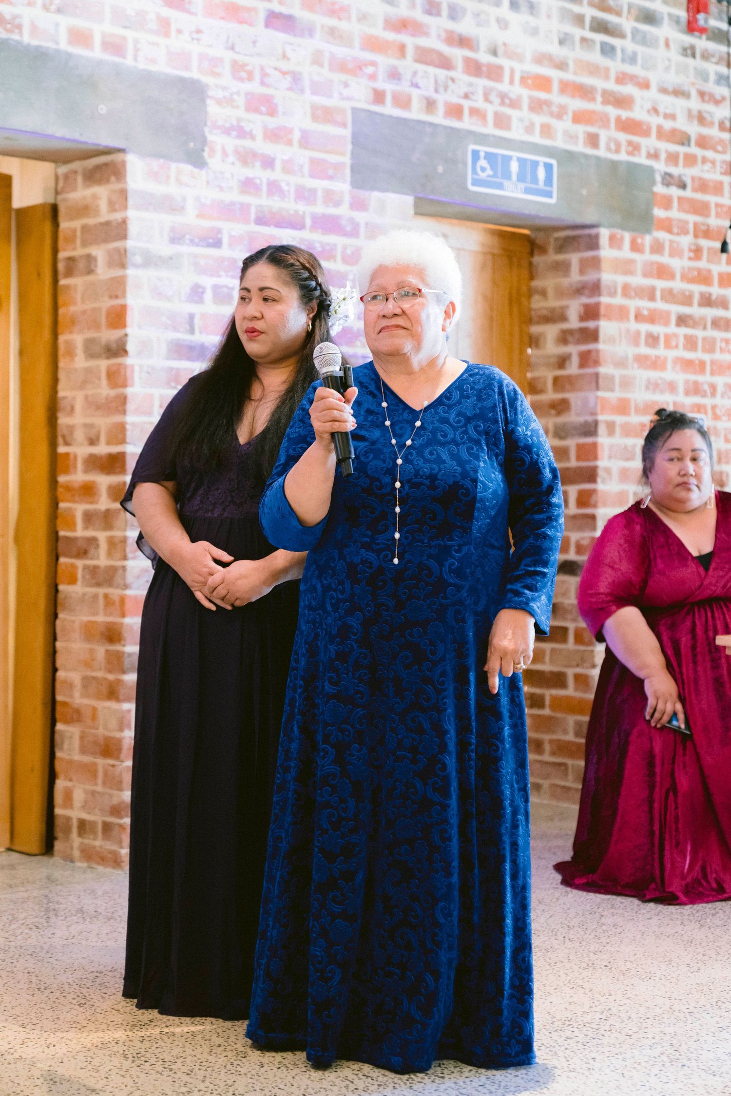Wedding guests in formal attire gather near a brick wall during reception celebrations.