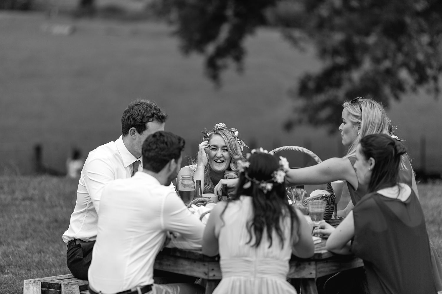 Group of people having a casual outdoor picnic gathering in a park setting at sunset, shown in black and white.