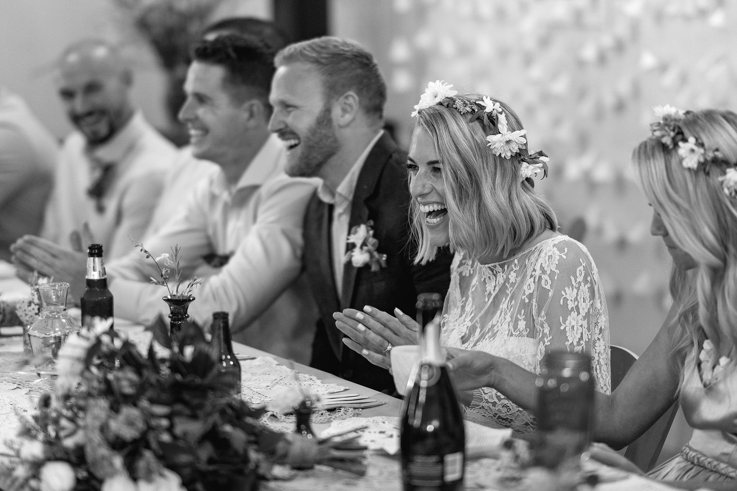 Wedding guests enjoying a meal and drinks together at a sunny outdoor reception celebration with wine glasses and flowers.
