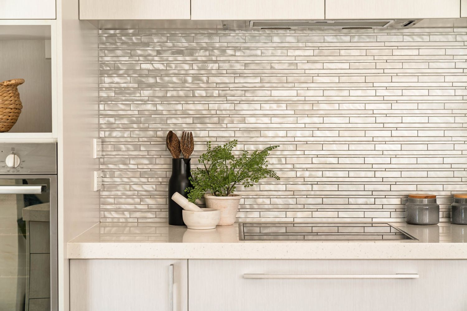Minimalist white kitchen featuring textured tile backsplash, sleek cabinet handles, and potted fern decor.
