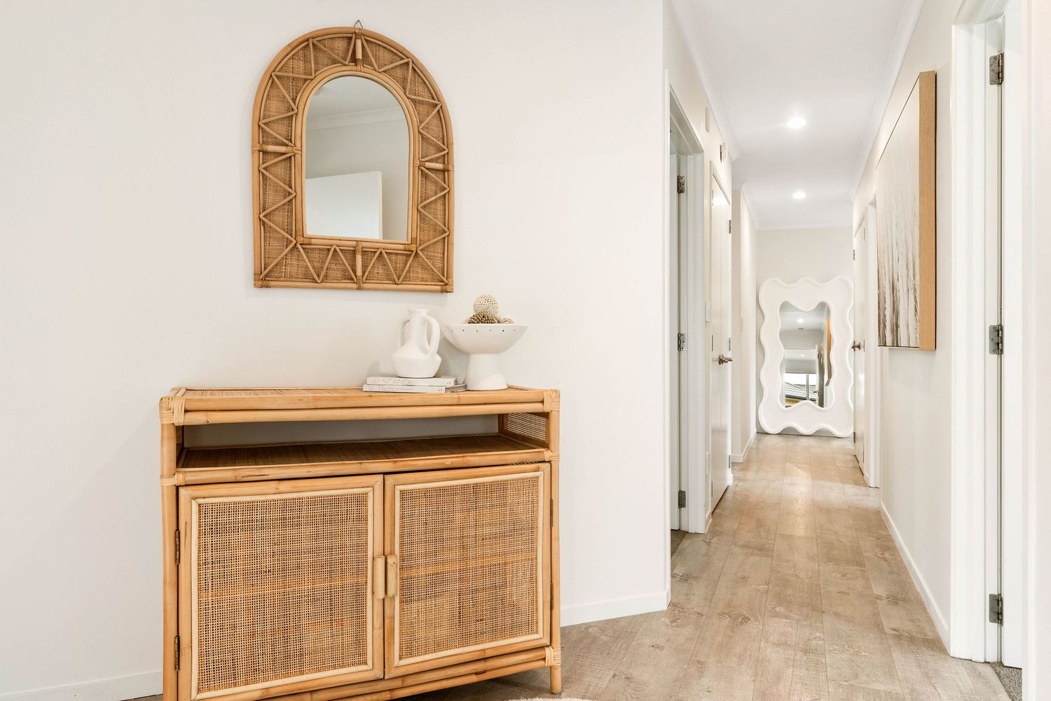Hallway with white walls features a wooden console table and decorative gold mirror, leading to multiple closed doors.
