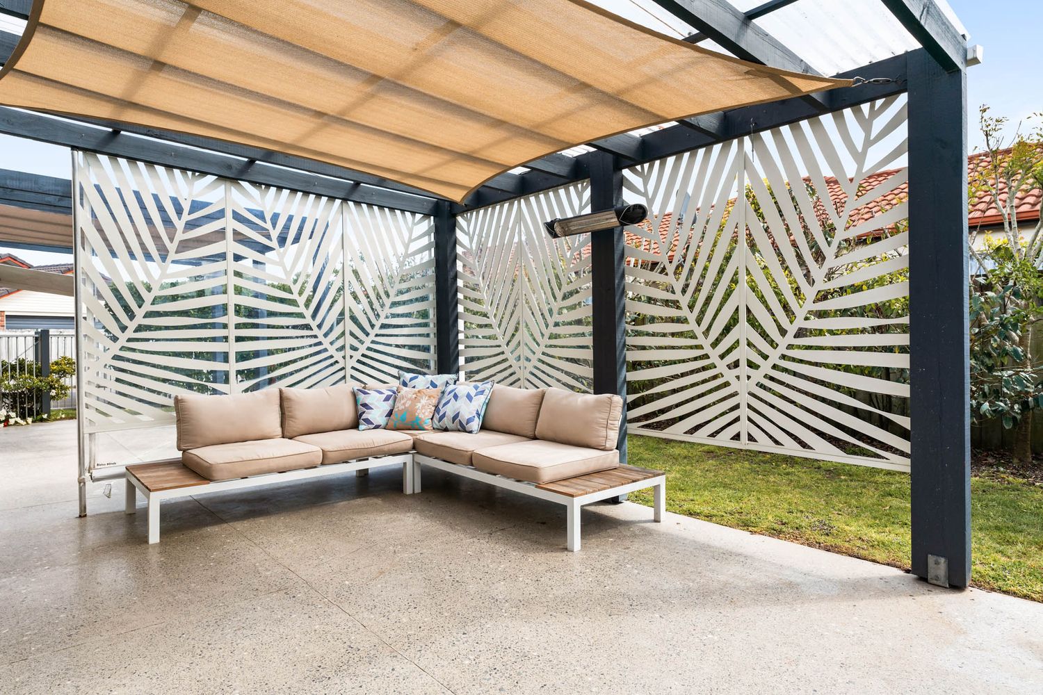 Modern outdoor patio space with L-shaped seating and decorative palm leaf privacy screens under pergola.