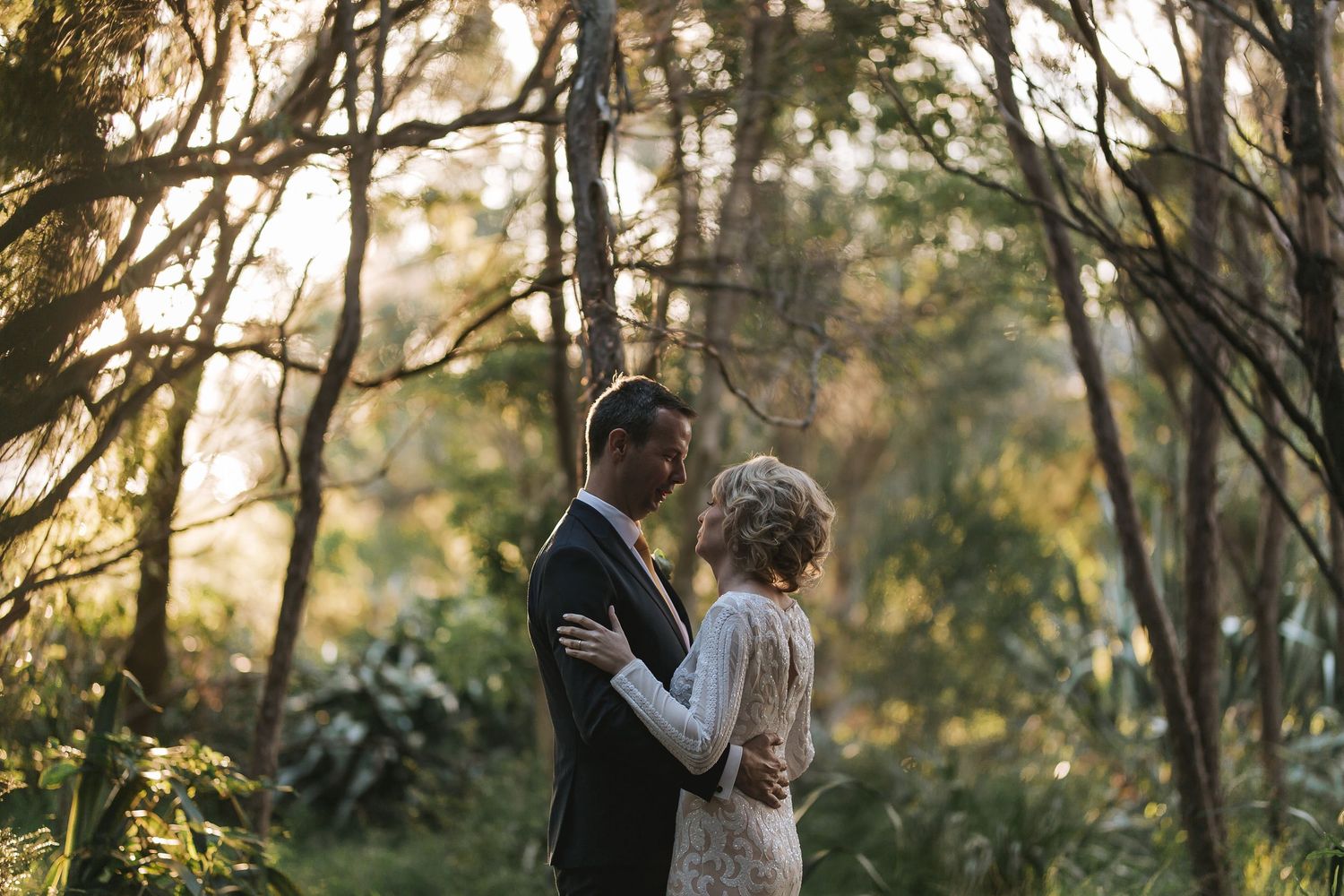 A couple embraces intimately in a sunlit wooded area during their outdoor photo session.
