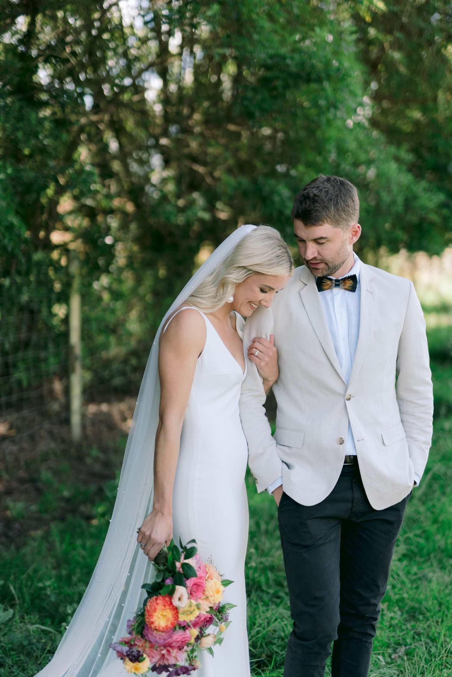 A romantic outdoor wedding portrait with a couple in elegant attire holding a colorful floral bouquet.