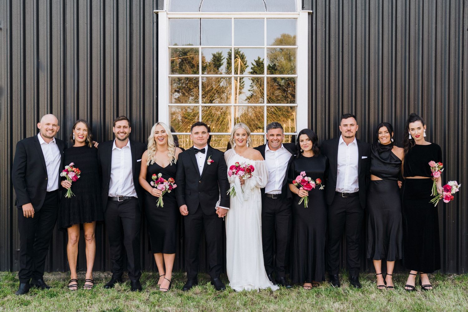 A formal wedding party portrait with black and white attire against a dark metal wall.